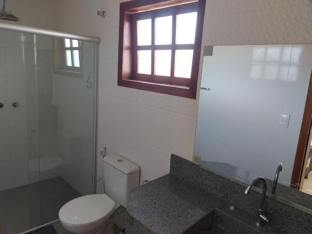A bathroom with a glass shower enclosure, a toilet, a sink with a mirror, and a window above the sink.