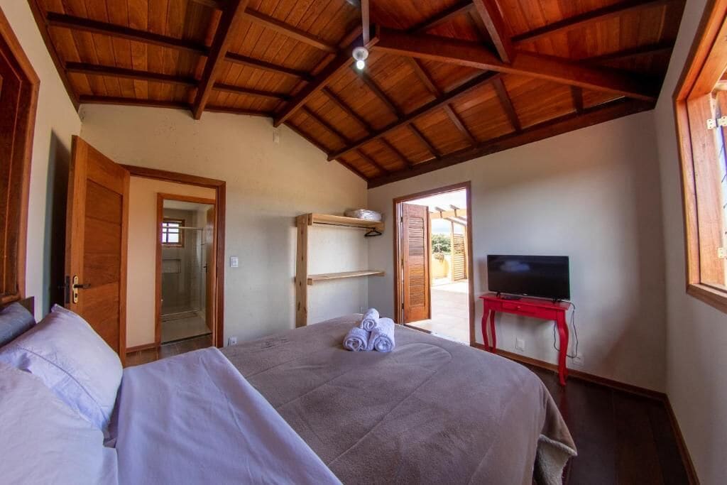 A bedroom with a bed, a television on a stand, and a door leading to an outdoor area.