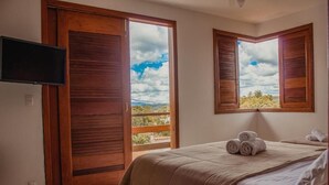 A bedroom with a bed, a television, and a balcony with wooden shutters. - Soham Guest House (Diamantina)