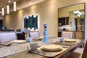 A dining table set with plates, cups, and cutlery, with a decorative vase and a wall art piece in the background. - Ocean View Copala Condo | 3BR | Huge Balcony, Grill & Firepit (Cabo San Lucas)