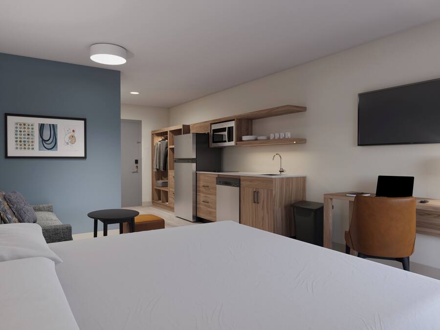 Una habitación de hotel moderna con una cama grande, un escritorio con computadora, un microondas y un televisor de pantalla plana.