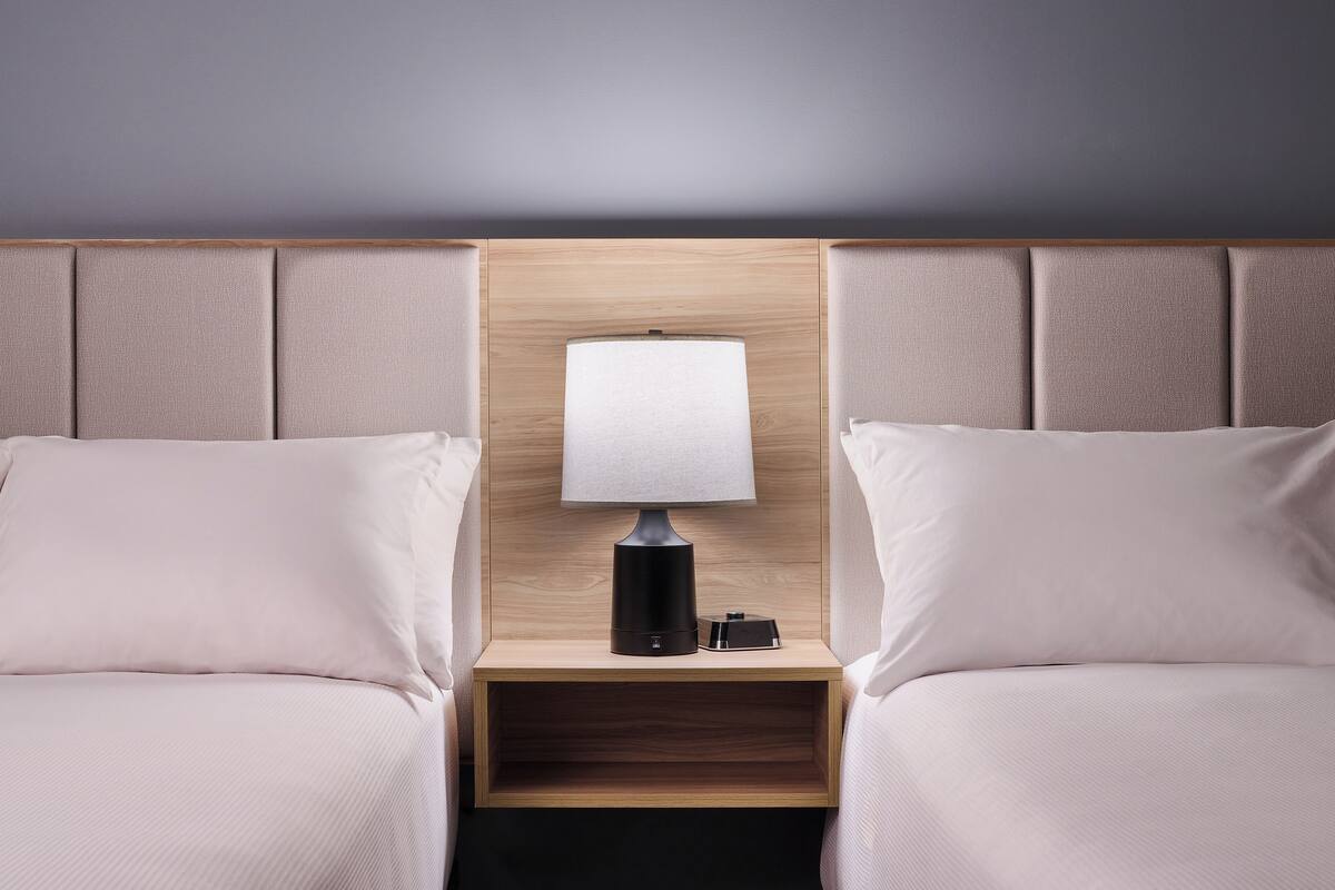 A hotel room with two beds, a nightstand with a lamp, and a wooden headboard.