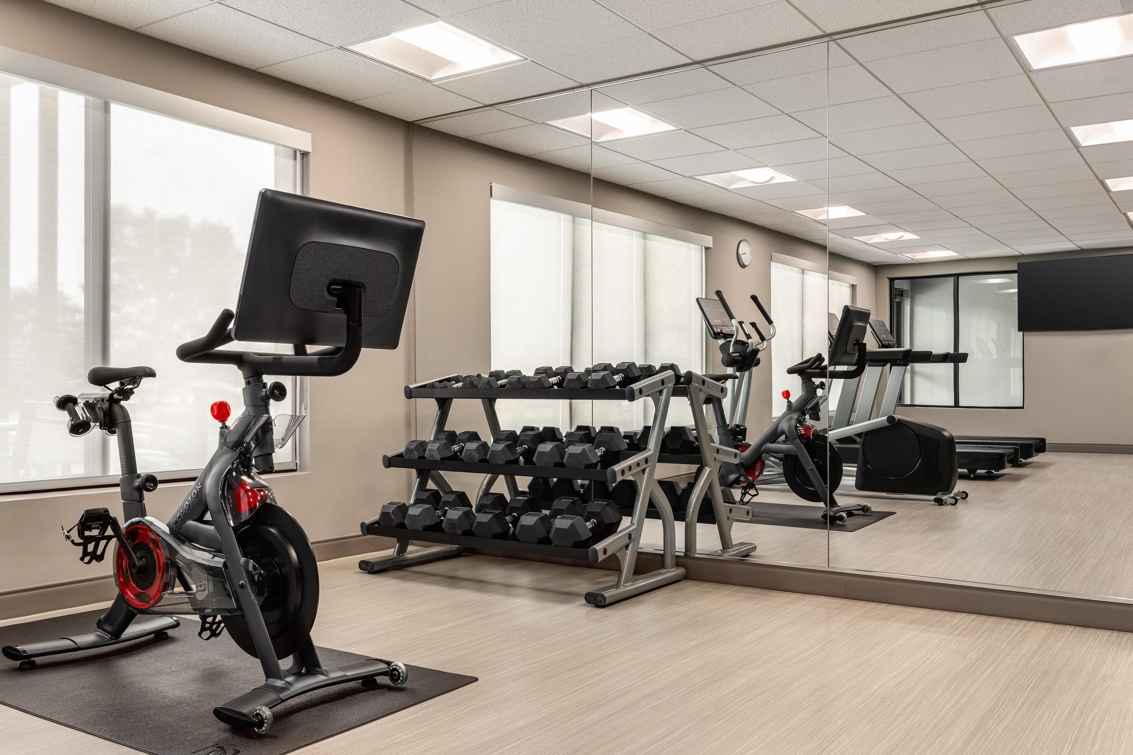 A gym with exercise equipment, a mirror, and large windows.