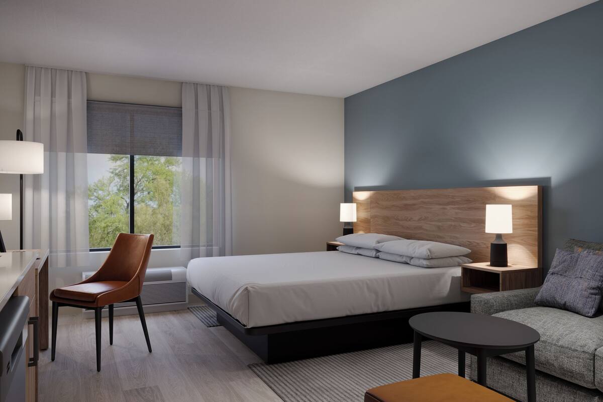 A hotel room with a bed, a desk, a chair, a sofa, and two bedside lamps.