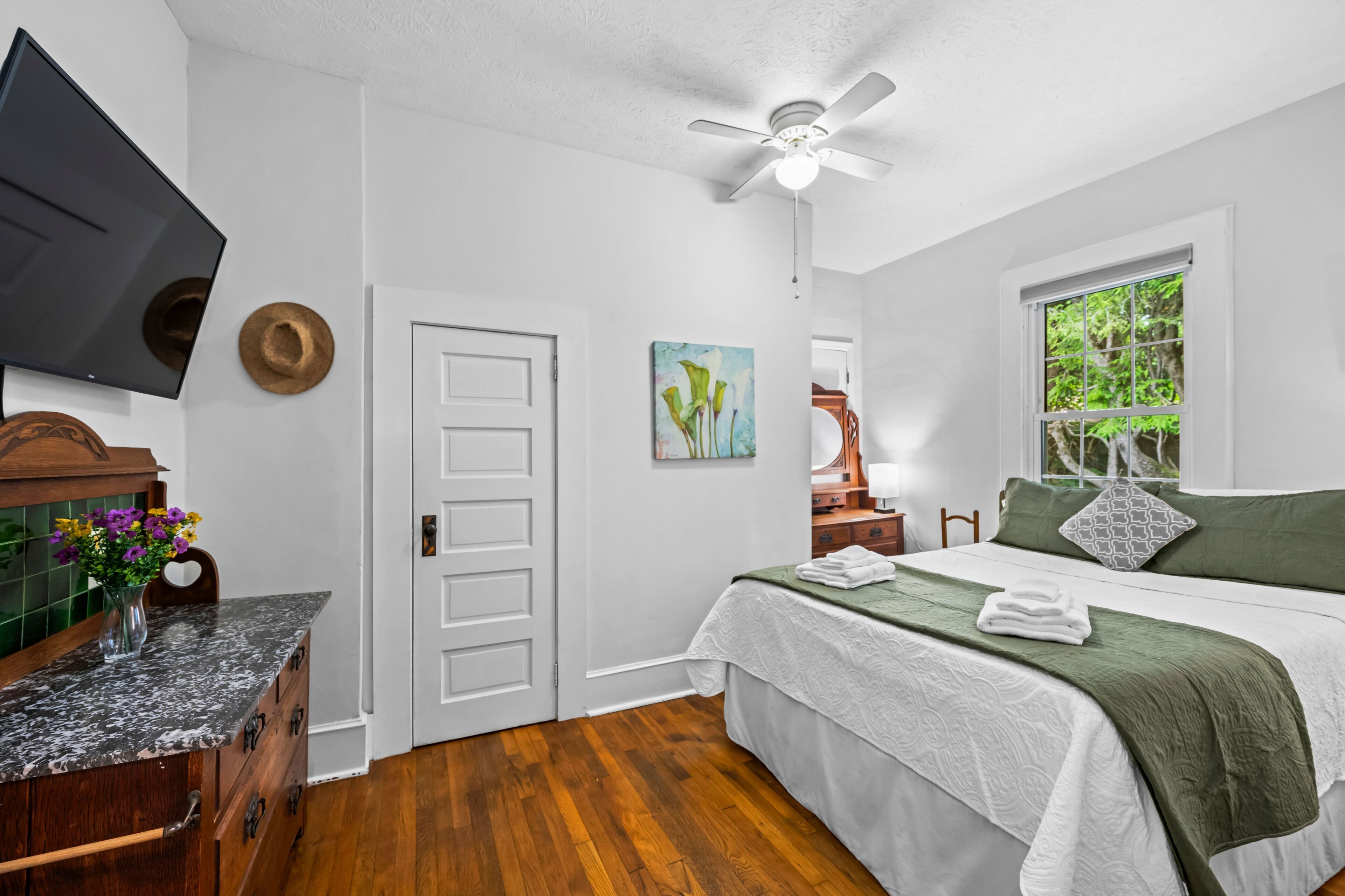 A bedroom with a bed, a television, a ceiling fan, a window, and a door.