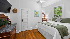 Un dormitorio con una cama, televisor, ventilador de techo, ventana y puerta.