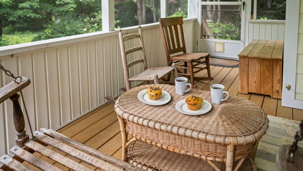 Una mesa de mimbre con dos platos de muffins y dos tazas blancas sobre una terraza de madera.