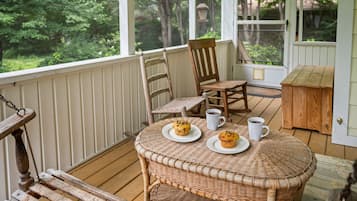 Une table en osier sur laquelle sont posées deux assiettes de muffins et deux tasses blanches, le tout sur une terrasse en bois.