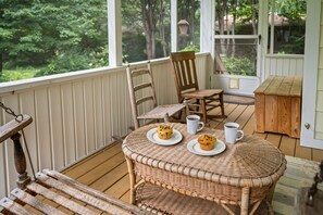 A wicker table with two plates of muffins and two white mugs on a wooden deck. - Walk to Brevard | Fenced Yard + Relaxing Porch (Brevard)