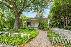 A single-story house with a front porch, surrounded by a gravel driveway and a white picket fence. - Walk to Brevard | Fenced Yard + Relaxing Porch (Brevard)