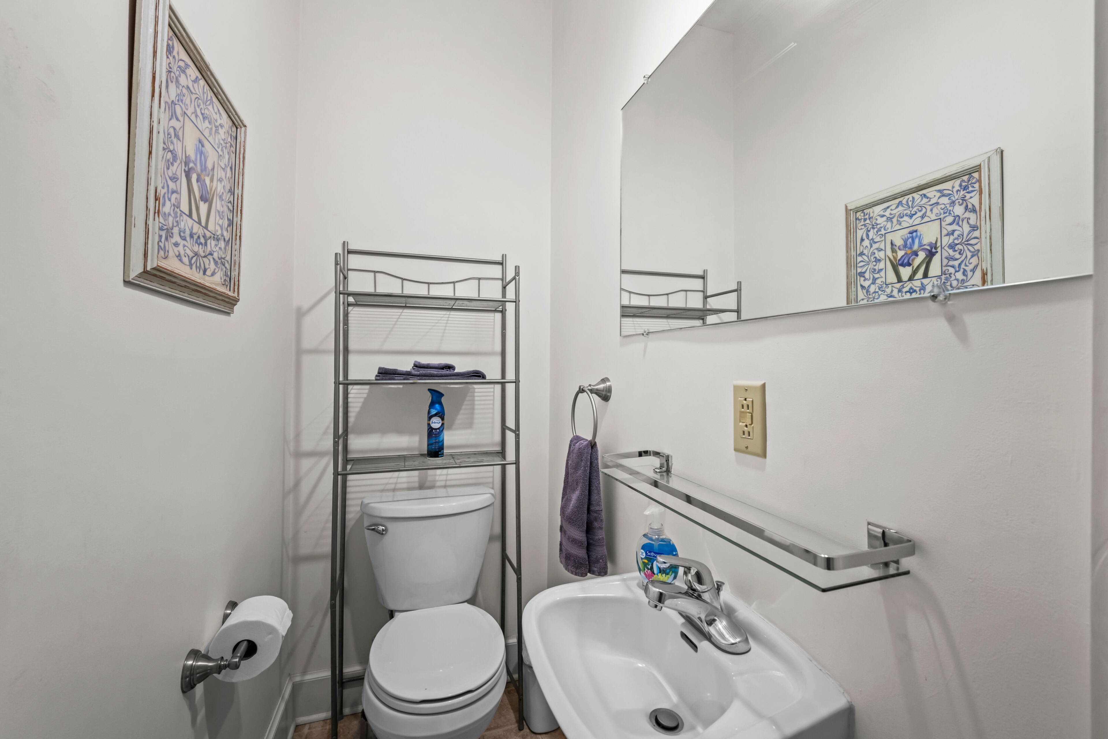 Un baño con inodoro, lavabo, espejo y estante con artículos de aseo.