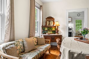 A room with a sofa, wooden dining table, kitchen area, and a view of the outdoors. - Walk to Brevard | Fenced Yard + Relaxing Porch (Brevard)