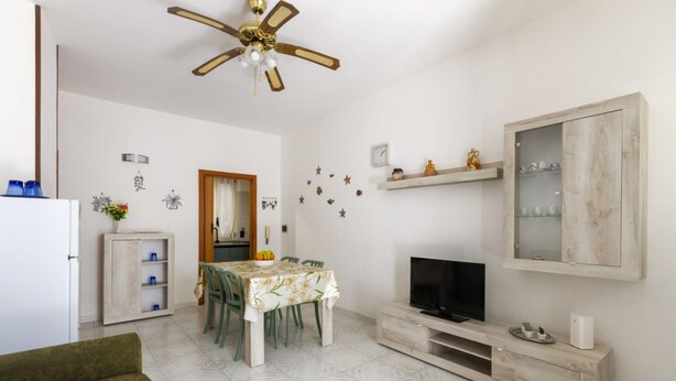 A living room with a dining table, chairs, a TV, a cabinet, and a ceiling fan. - This colorful and welcoming apartment, ideal for up to 4 people, is strategically located in Lecce: outside the restricted traffic zone but just steps from the historic center. Just 400 meters from Porta San Biagio, it's easy to immerse yourself in the w (Otranto)