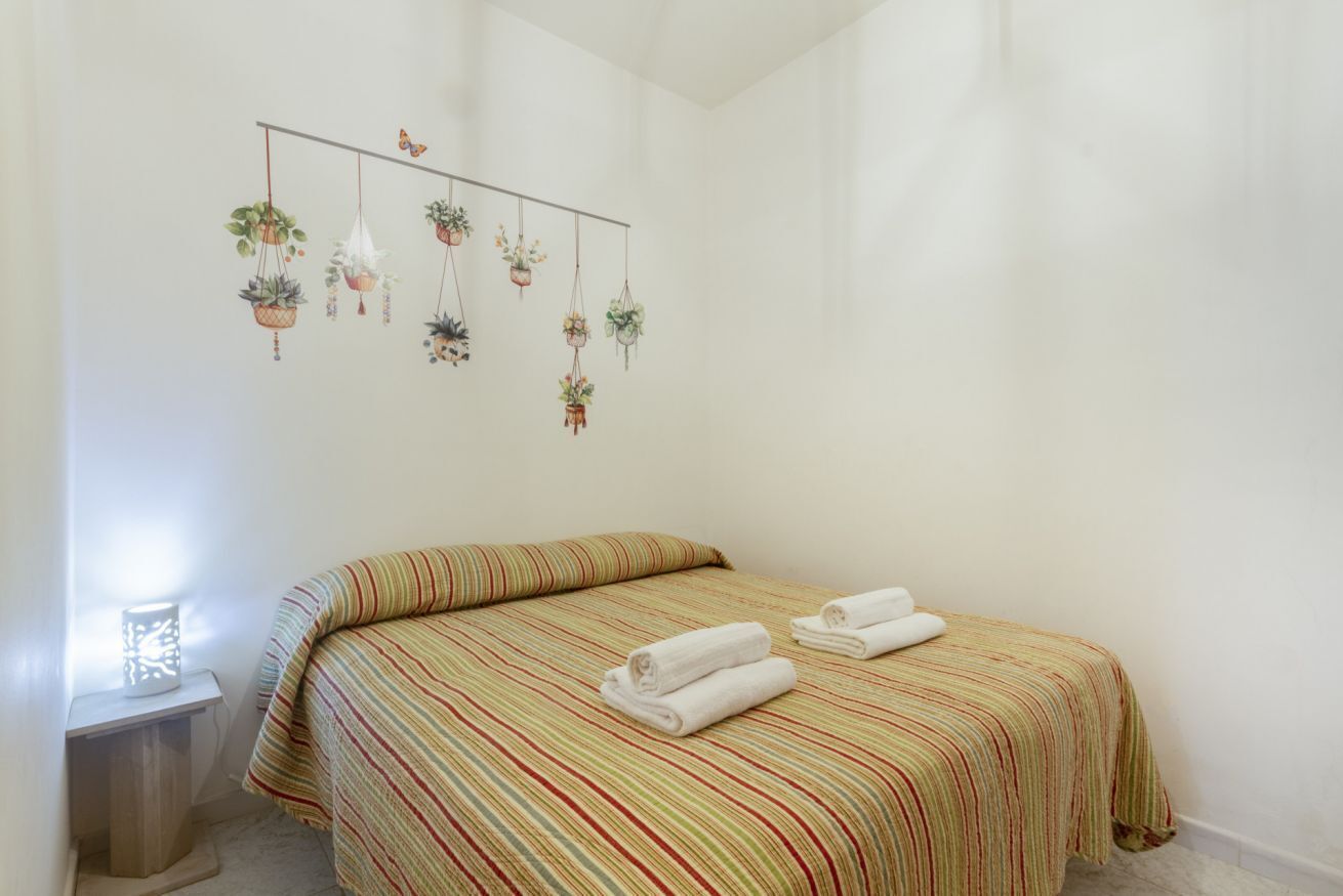 Ein Zimmer mit einem Bett, gestreifter Bettwäsche, einer hängenden Pflanzengruppe und einer Nachttischlampe.