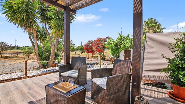 Eine Terrasse im Freien mit Korbmöbeln, einer Pergola und Blumentöpfen.