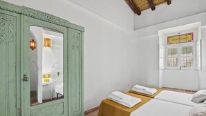 Ein Zimmer mit einem grünen Schrank, zwei Betten mit weißen Bettwäsche, einem Fenster mit Aussicht und einem kleinen Tisch mit Handtüchern.
