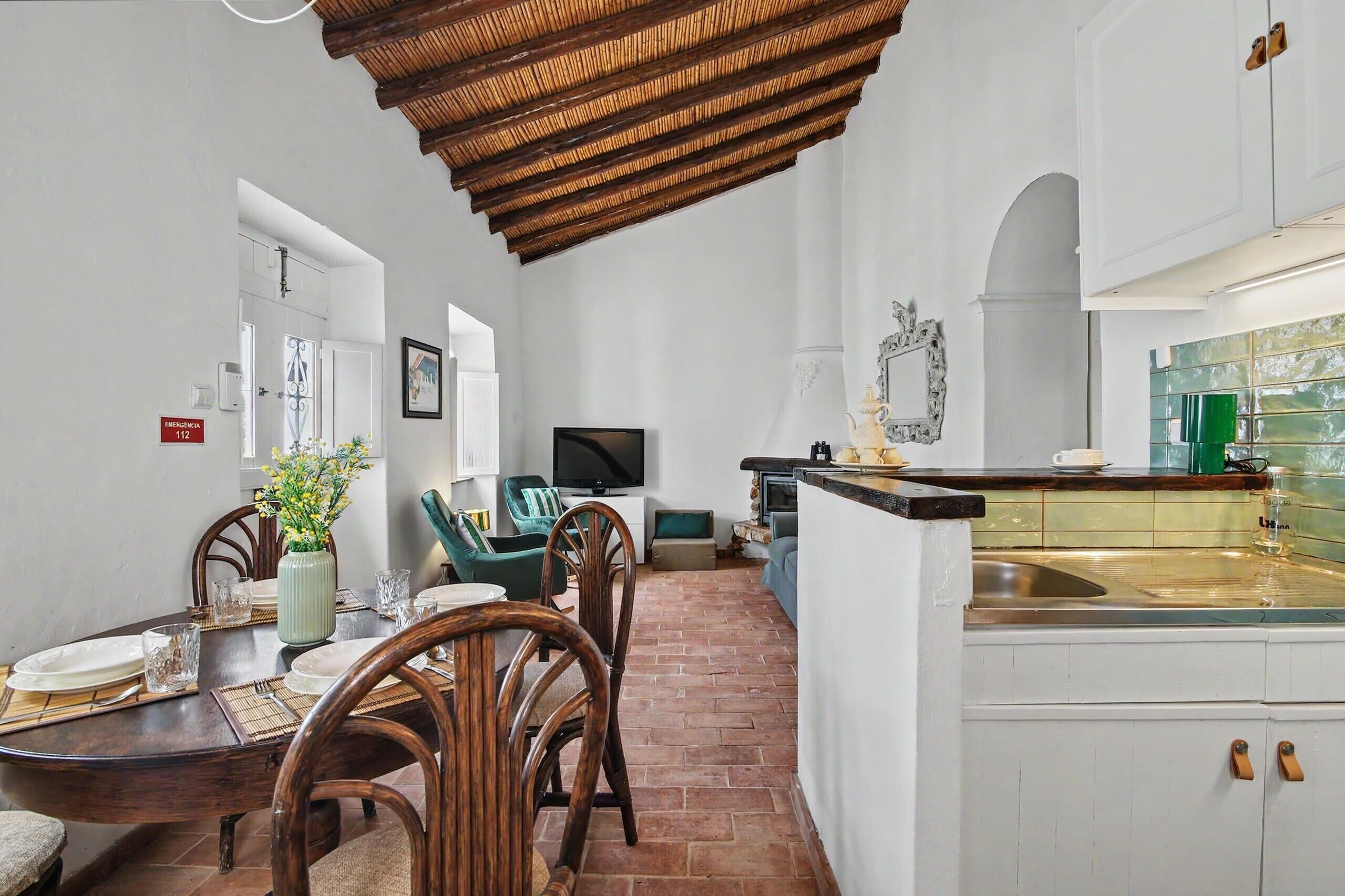 A kitchen with a tiled backsplash, a dining area with a table set for two, and a television in the background.
