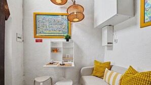 Una stanza con un divano bianco, un tavolino con due sedie, una mappa incorniciata appesa al muro e uno scaffale con oggetti decorativi.