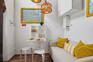 Una habitación con un sofá blanco, una mesita con dos sillas, un mapa enmarcado en la pared y una estantería con adornos.