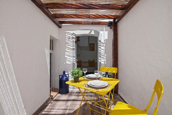 A narrow corridor with a table set for two, yellow chairs, a potted plant, and a blue gas cylinder.