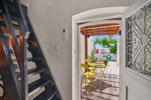 Una escalera conduce a un cuarto con vista a un espacio exterior, una mesa con sillas y un ventanal con detalles de hierro forjado.