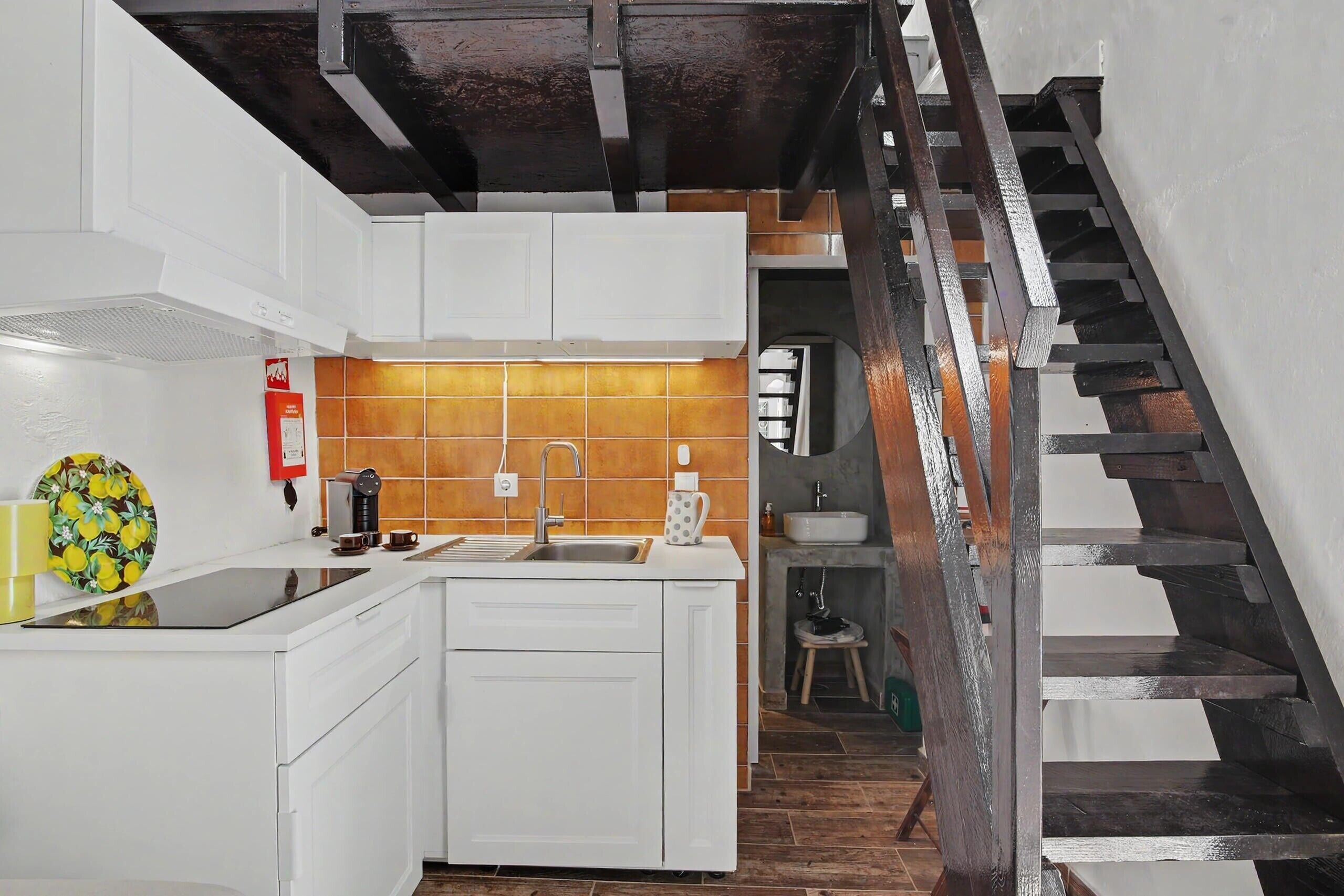 Une cuisine avec des meubles blancs, un évier et une machine à café. On y trouve un escalier avec des marches en bois et une rampe en métal.