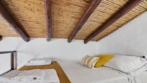 Una stanza con soffitto alto, travi in legno, un letto con biancheria bianca e un cuscino giallo, e una finestra con vista.