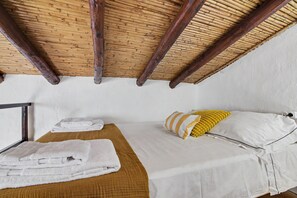 Una habitación con techo alto, vigas de madera, cama con ropa de cama blanca y almohada amarilla, y ventana con vistas.