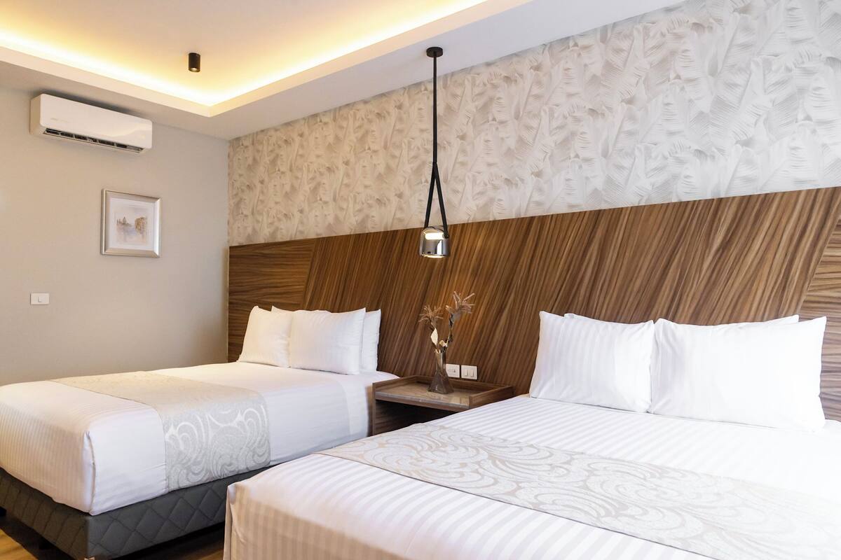 A hotel room with two beds, a wooden headboard, a wall-mounted air conditioner, and a framed picture.