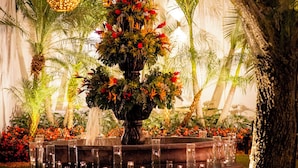 Un jardín con un arreglo floral central, palmeras y luces esféricas colgantes.