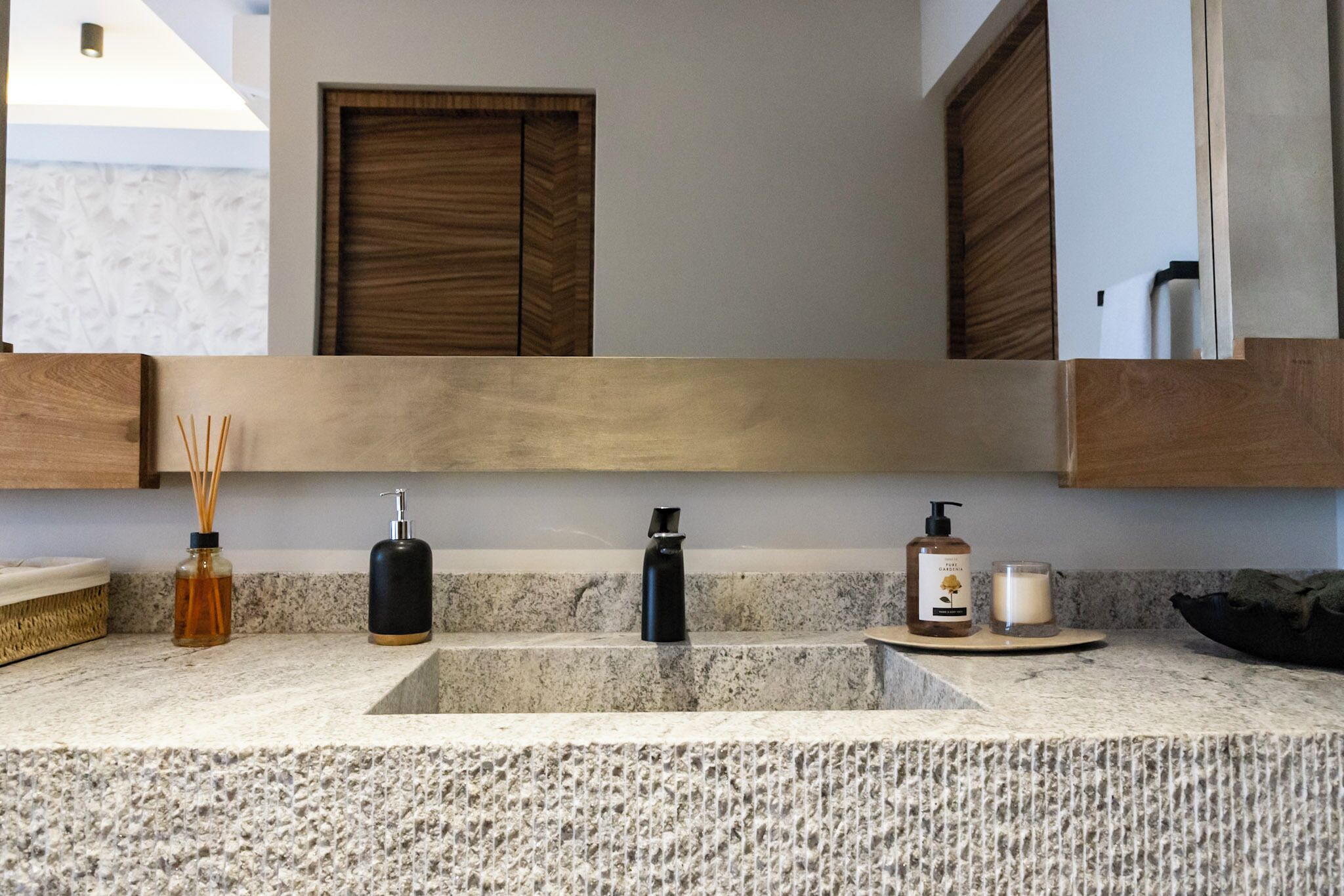A bathroom with a granite countertop, a wooden vanity, a mirror, and a towel rack.