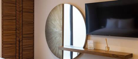 A modern hotel room with a large mirror, a mounted television, and a wooden wardrobe.