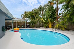 Ein Schwimmbad mit Holzterrasse, einer überdachten Veranda und verschiedenen tropischen Pflanzen.