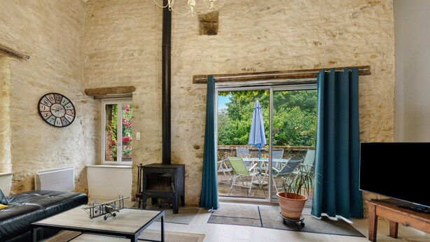 A living room with a fireplace, a sofa, a TV, and a view of the outdoors. - Gîte Les Magnolias Logis Bourseguin, private terrace and Wi-Fi (Bourneau)