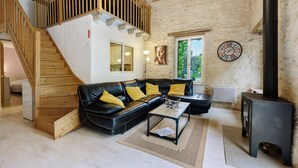 A living room with a wooden staircase, a black leather sofa, a coffee table, and a black wood-burning stove. - Gîte Les Magnolias Logis Bourseguin, private terrace and Wi-Fi (Bourneau)