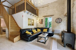 Ein Wohnzimmer mit einer Holztreppe, einem schwarzen Ledersofa, einem Couchtisch und einem schwarzen Kaminofen.