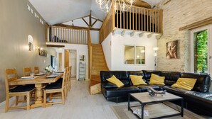 A spacious living area with a wooden dining table, black leather sofa, and a staircase leading to an upper level. - Gîte Les Magnolias Logis Bourseguin, private terrace and Wi-Fi (Bourneau)