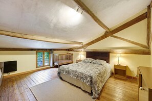 Ein Schlafzimmer mit Bett, Holzbalken, Fernseher, Nachttisch, Lampe und einem Fenster mit Aussicht.