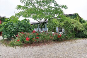Ein Gebäude mit traditioneller Ziegeldach, umgeben von üppigem Grün und blühenden Pflanzen.