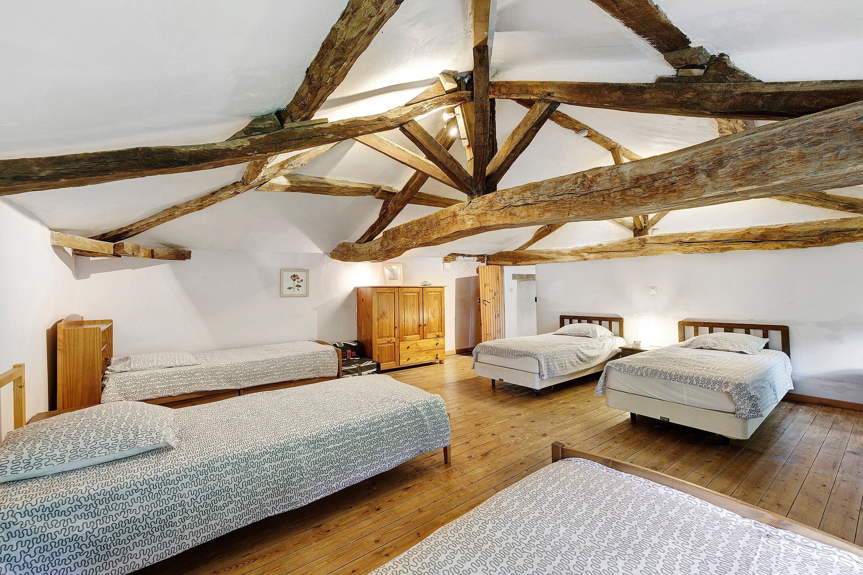 A rustic room with exposed wooden beams, three beds with patterned bedding, wooden wardrobe, and a wooden floor.
