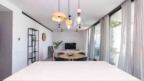 Una cocina moderna con una isla grande, luces colgantes, un comedor con una mesa redonda y un televisor al fondo.