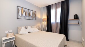 Un dormitorio con una cama, una mesita de noche, una lámpara, un estante y una obra de arte en la pared.