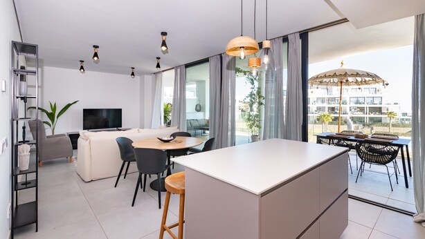 Un apartamento moderno con una isla de cocina, comedor y un balcón con sombrilla.
