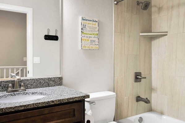 A bathroom with a granite countertop sink, a toilet, a shower with a handheld showerhead, and a wall-mounted sign with bathroom rules. - Perfect Family Getaway with Pool, Lazy River & Gym (Hurricane)