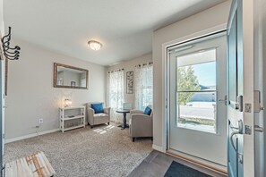 Ein Zimmer mit Tür, zwei Stühlen, einem kleinen Tisch, einem Spiegel und einem Fenster mit Vorhängen.