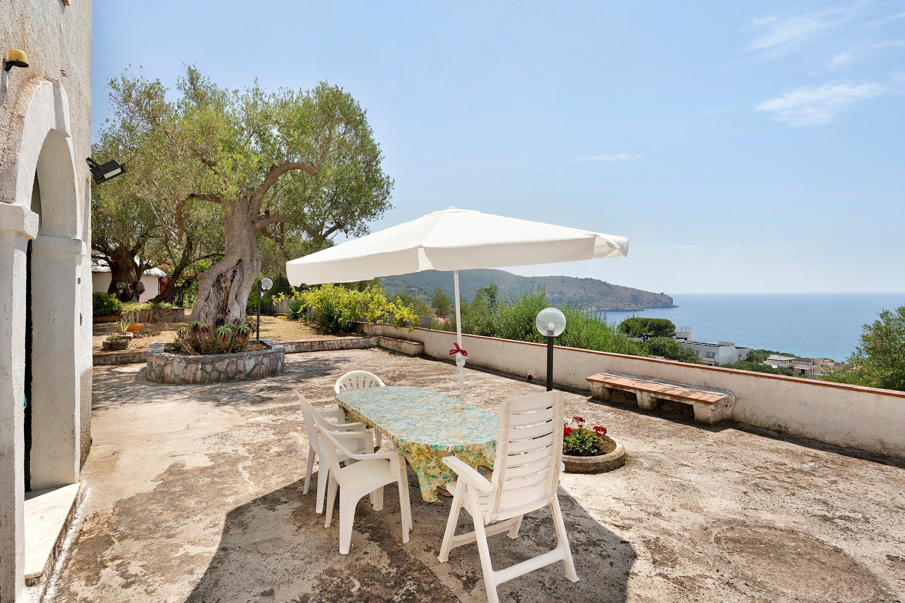 Eine Terrasse mit Tisch und Stühlen, einem Sonnenschirm und Blick aufs Meer.
