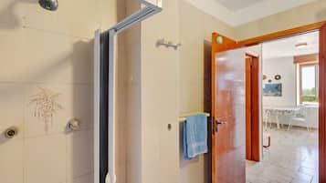 A bathroom with a shower, a towel rack, and a door leading to a dining area.