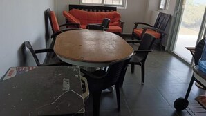 A room with a round table, several chairs, a sofa, and a view through a glass door.
