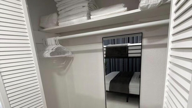 Een inloopkast met een spiegelkast, planken met opgevouwen handdoeken en een kledingroede.