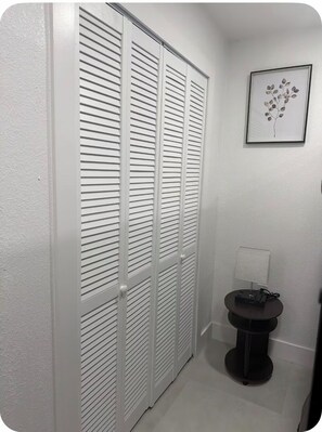 A hallway with a white closet, a framed plant, and a small table with a lamp. - Chic Private Suite for 6 near USF & Busch Garden (Tampa)